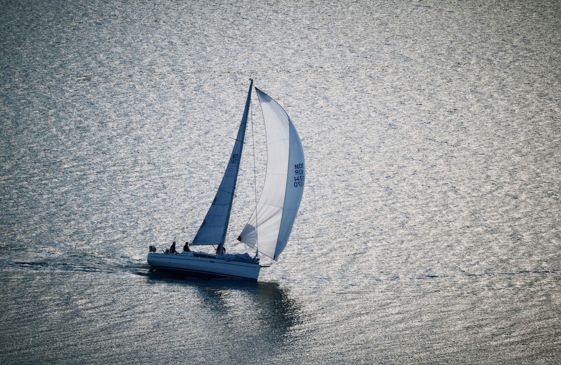 A sailboat moving across sunlit water with its sails raised